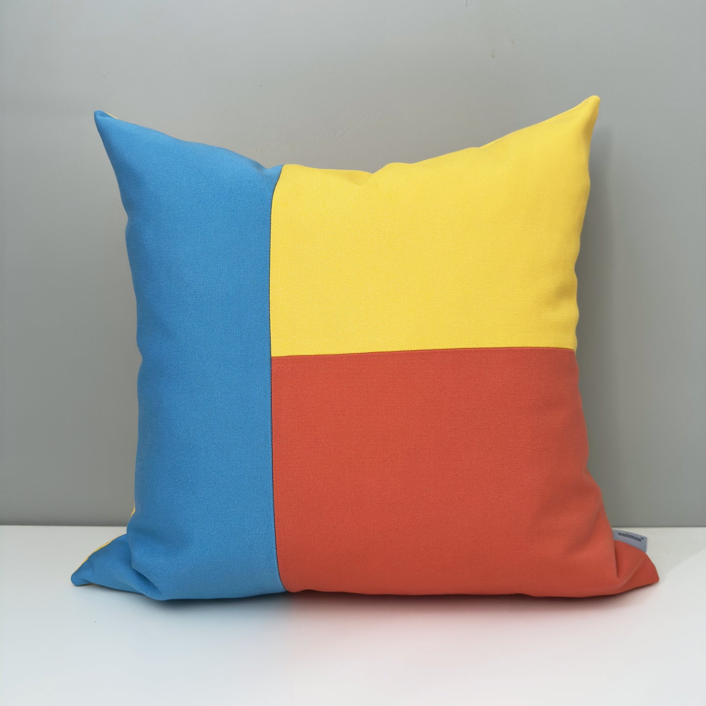 Color-blocked outdoor pillow with blue, yellow, and orange sections for a modern nursery or patio